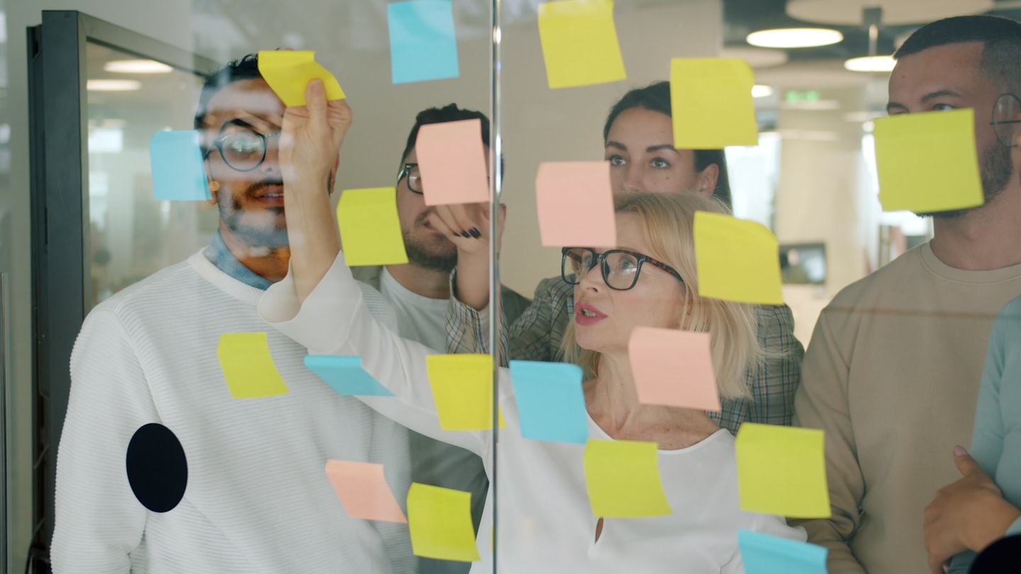 Business team brainstorming with sticky notes on glass wall.