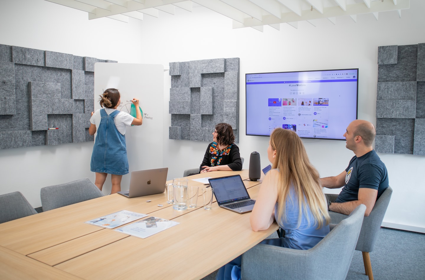 Team collaborating around a table and whiteboard in a bright office.
